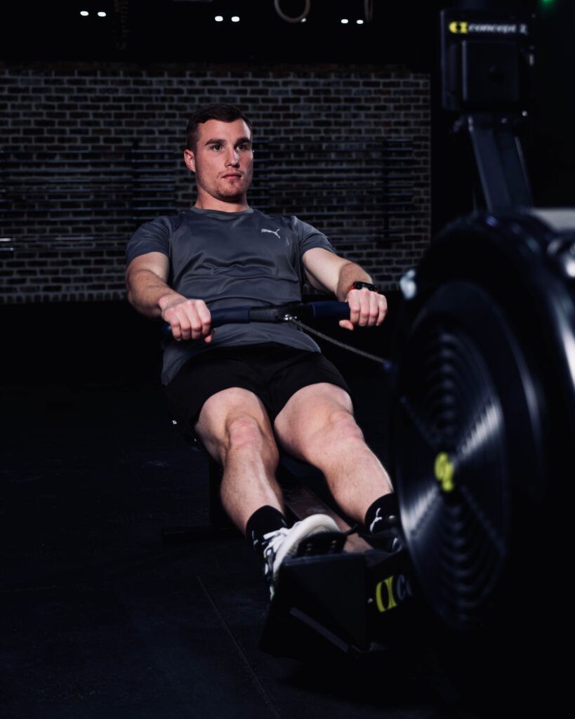 Athlete performing a rowing workout on a Concept2 rowing machine at Willow Way Fitness Gym as part of HYROX PFT test training, focusing on strength, endurance, and performance preparation.